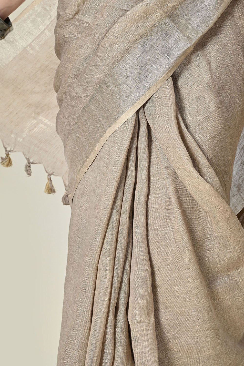 Elegant grey linen saree with tassels, dyed organically with pomegranate, enhanced by gold accents and handwoven details; suitable for dry cleaning.